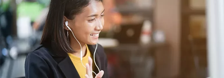 Woman wearing earbuds, smiling in a cafe during a video call.